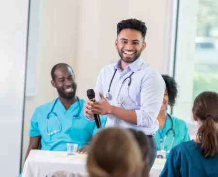 Young male physician speaking to room of healthcare providers