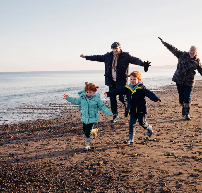 Grandparents running like airplanes on beach with little boy and girl